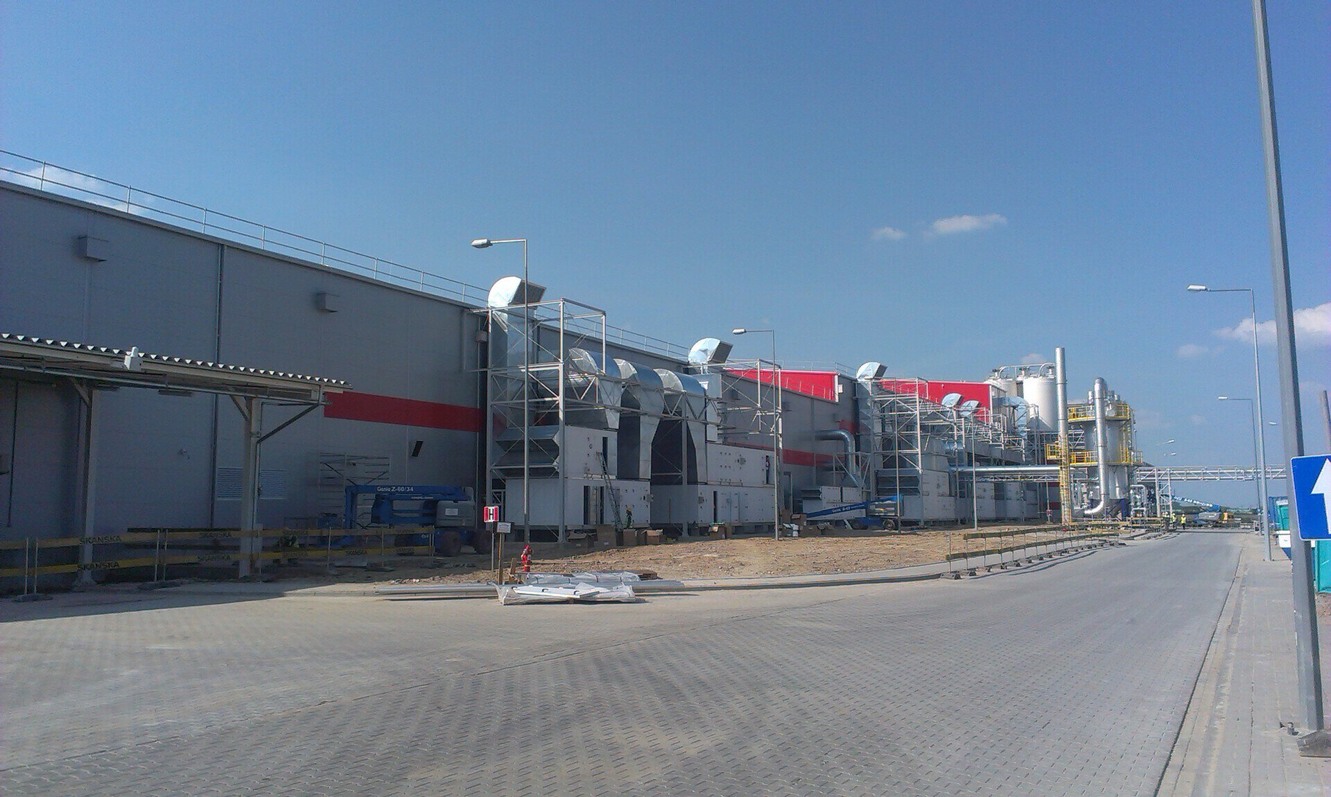 Fațadă cu zonă de andocare la fabrica Kellogg’s Pringles din Kutno, panouri sandwich albe cu accente roșii orizontale specifice brandului și uși de andocare roșii, șantier Skanska, proiect PPAE